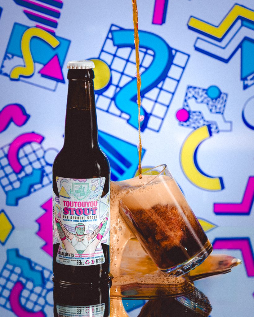 une bouteille 33 cl de bière Toutouyoustout de la brasserie Sainte Cru Colmar avec un verre qui se remplit et déborde de cette bière brune avec un fond des années 1980