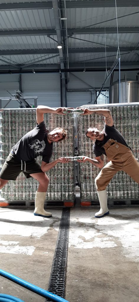 2 brasseurs en train de réaliser une FUSION à la Dragon Ball Z avec des canettes de bière Blitzkrieg Hop de la brasserie Sainte Cru devant des palettes remplis de cans